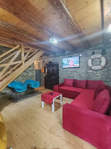 dnevna soba na kojoj se vidi tv, crvena ugaona garnitura, dve plave fotelje i kredenac