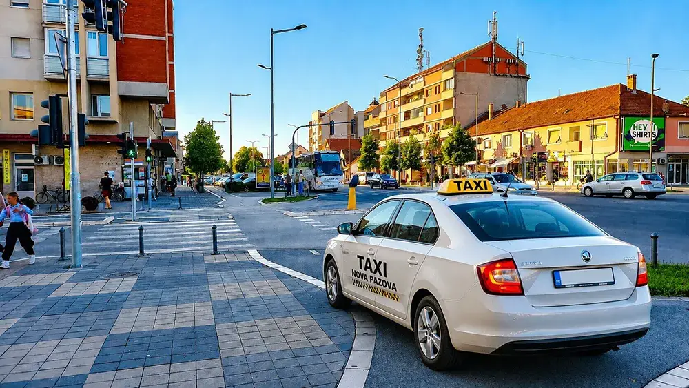 Taxi Nova Pazova vozilo parkirano na modernoj gradskoj raskrsnici u centru Nove Pazove, saobraćaj, autobusi i pešaci tokom sunčanog dana
